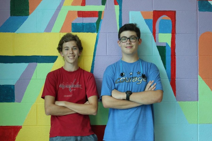 Topher Wagner and Charlie Schiavo pose boldly in front of a colorful painting.
